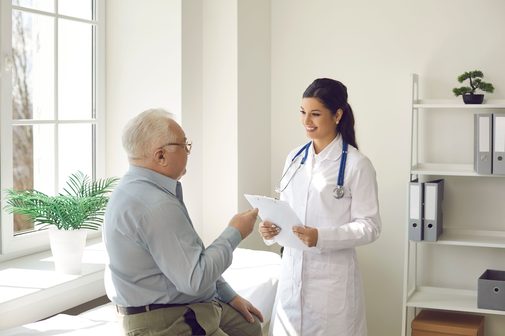 Smiling doctor listening to senior patient who's sitting on examination bed in her office